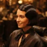 Woman with short blunt 1920s bob and finger-waved sides in an old-fashioned salon chair under warm tungsten light