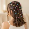 Back three quarter view of a woman with small butterfly clips scattered through a half-up section in bright even studio light