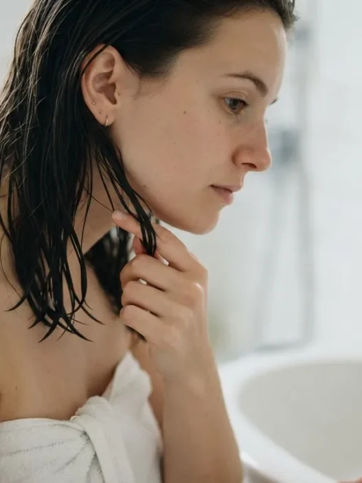 Woman testing dampness of freshly washed hair by pressing strand between fingertips at bathroom basin in bright light