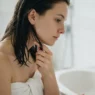 Woman testing dampness of freshly washed hair by pressing strand between fingertips at bathroom basin in bright light