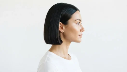 Woman with blunt chin-length french bob haircut seen in side profile against white studio background