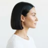 Woman with blunt chin-length french bob haircut seen in side profile against white studio background