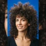 Woman with a full heavy chemical perm creating maximum curl volume, shot against a cobalt blue backdrop in bright studio light