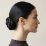 Woman in side profile wearing sleek low nape chignon against pale backdrop, crown to collarbone framing