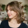 Woman with square nineties layered cut and claw clip crown showing face-framing curtain bangs falling freely forward