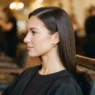 Woman with smooth side-parted hair sitting in a vintage salon chair under warm tungsten light, ready to be set
