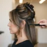 Woman with shoulder-length hair in large top section clipped up before blowout, lower panels loose, bright working light