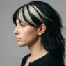 Woman with bold chunky highlights and dramatic side-swept fringe in side profile against grey backdrop
